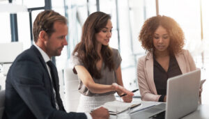 Business people, meeting with opinion and laptop, ideas in collaboration on project feedback with coaching. Teamwork, online review and research, man and women with target management in modern office.